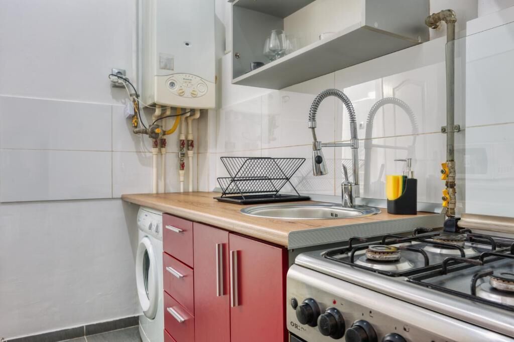 A kitchen with a washing machine, a sink with a hose, and a gas stove.