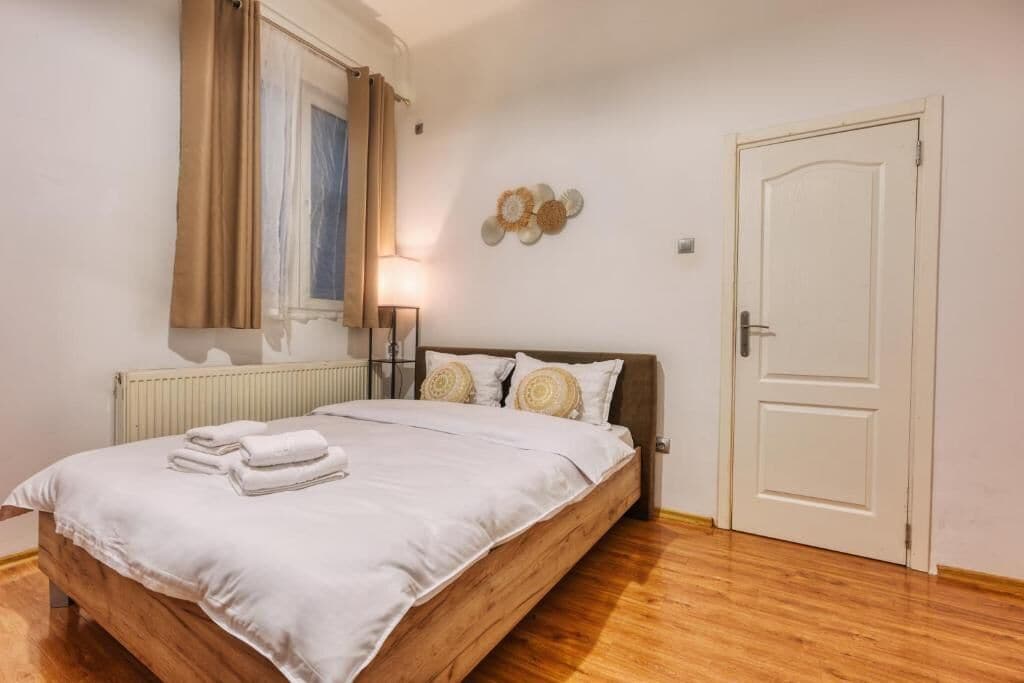 Ein Schlafzimmer mit einem hölzernen Bett, weißer Bettwäsche, einem Heizkörper, einer Tür und einem Wandbild.
