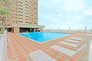 Ein Pool mit Liegestühlen, ein Gebäude mit mehreren Balkonen und ein klarer Himmel.