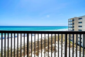 A beach view with a balcony railing, sandy beach, and a building with multiple floors. - Pinnacle Port C1-503 (Panama City Beach)
