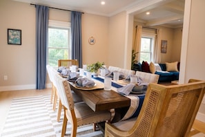 A dining area with a wooden table set for six, surrounded by wicker chairs. - Lakewind House - sauna, hot tub, 5 min to Lake (Barnstable)