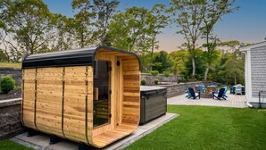 Een houten sauna met een gebogen dak, een ingebouwde bank en een terras met tuinmeubilair.
