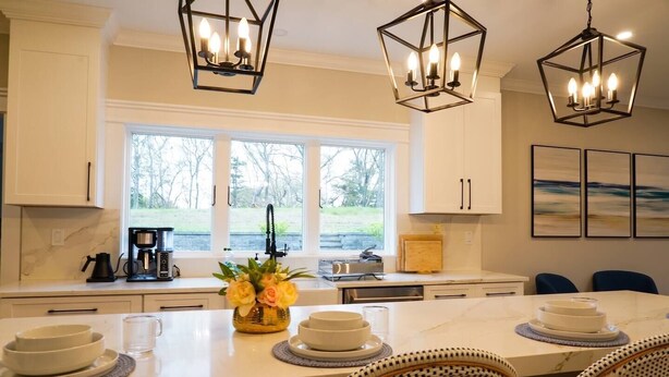 Een keuken met witte kasten, een groot eiland met een bloevas en hanglampen.