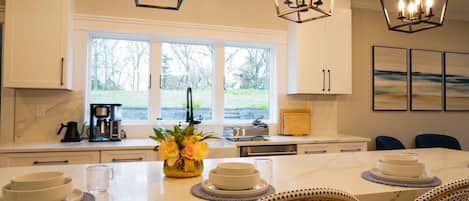 A kitchen with white cabinets, a large island with a vase of flowers, and pendant lights.