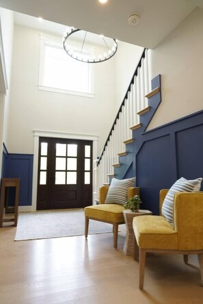 A spacious room with a staircase, a large window, and a chandelier. - Lakewind House - sauna, hot tub, 5 min to Lake (Barnstable)
