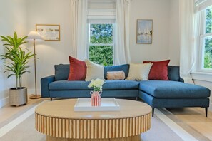 Un salon avec un canapé bleu, une table basse en bois, une plante en pot et deux tableaux accrochés au mur.