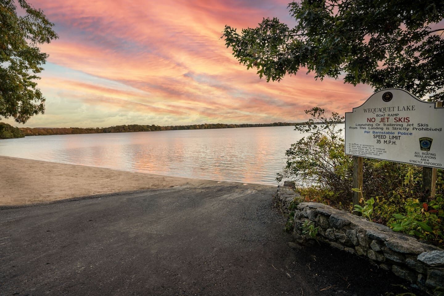 A sunset view at Wequaquet Lake with a sign prohibiting jet skis and a speed limit of 35 mph.