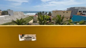 A yellow wall with a framed picture of a dish, a view of the ocean, and buildings in the background. - PLAYA FELIZ (Zihuatanejo)