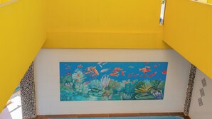 A swimming pool with a mural of marine life, surrounded by yellow walls and wooden flooring. - PLAYA FELIZ (Zihuatanejo)