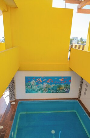 A swimming pool with a mural of marine life, surrounded by yellow walls and wooden flooring. - PLAYA FELIZ (Zihuatanejo)