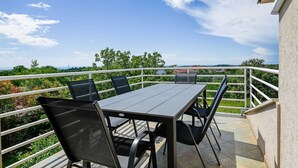 Un balcon avec une table et des chaises, une balustrade et une vue sur la verdure et les bâtiments.