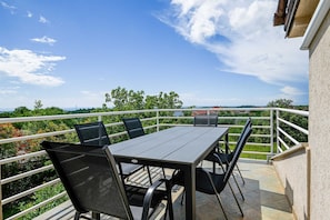 Ein Balkon mit Tisch und Stühlen, Geländer und Blick auf Grünflächen und Gebäude.