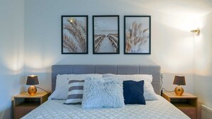 Une chambre à coucher avec un lit, deux tables de chevet et trois tableaux encadrés accrochés au mur.