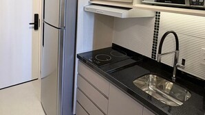 A modern kitchen with a built-in microwave, stainless steel refrigerator, and a black countertop.