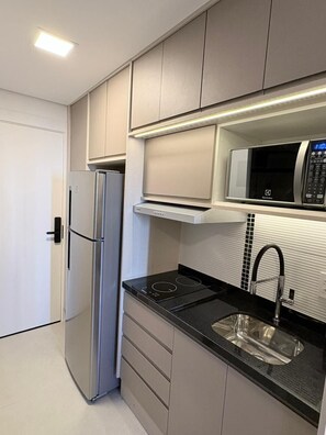 A modern kitchen with a built-in microwave, stainless steel refrigerator, and a black countertop.