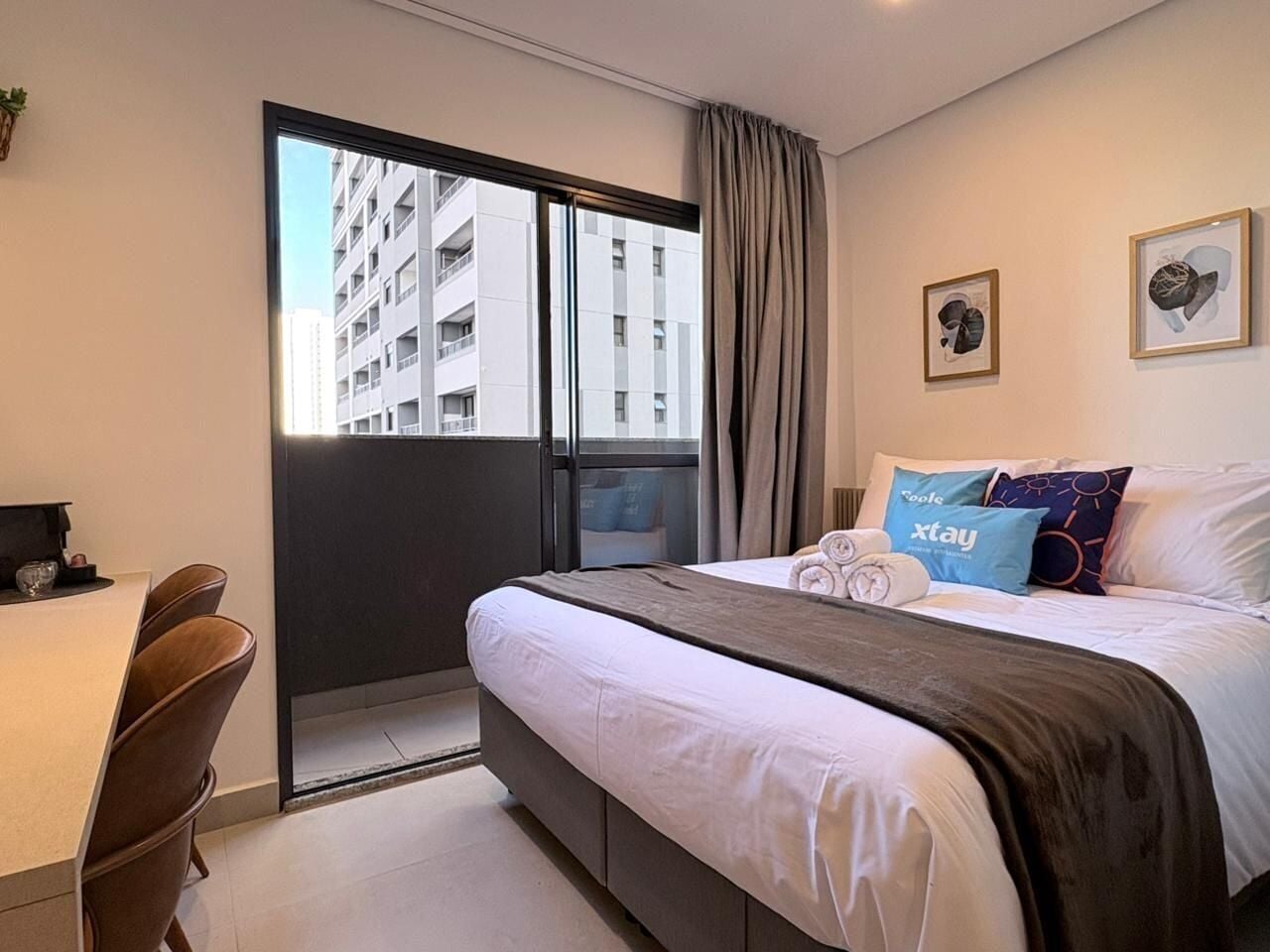 Habitación de hotel con cama, escritorio, silla y una ventana grande que ofrece vistas a un edificio.