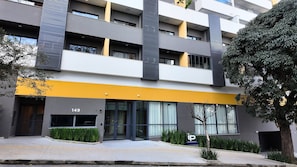A modern building with a yellow awning, numbered 149, featuring large windows and a small tree in the foreground.