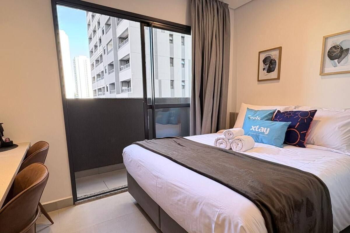 Hotellihuone, jossa on sänky, työpöytä ja suuri ikkuna, josta avautuu näkymä rakennuksiin.