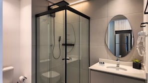 Casa de banho moderna com chuveiro envidraçado, espelho redondo e lavatório branco.