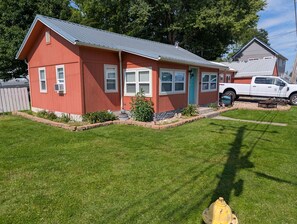 Ein rotes Einfamilienhaus mit grauem Dach, einer Veranda und einem kleinen Garten.