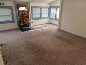 Ein Zimmer mit Teppichboden, einem Holzstuhl, einem kleinen Tisch und einer Tür mit Fenster.