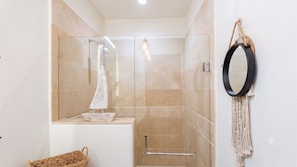 A modern bathroom with a glass shower enclosure, a towel rack, a mirror, and a wicker basket. - Luxury Vallarta Marina 1BR, 180° Balcony & Golf Views (Puerto Vallarta)