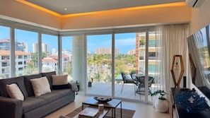 En moderne stue med sofa, sofabord og udsigt til en balkon med udendørs møbler.