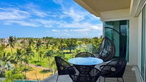 En balkon med et glasbord og stole, der vender ud mod en golfbane og palmer.