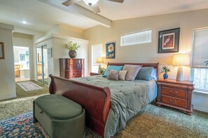 Een slaapkamer met een bed, nachtkastjes, een dressoir, een stoel en een raam met jaloezieën.