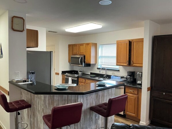 A kitchen with a central island, wooden cabinets, a microwave, and a refrigerator. - Beachside Vacation Home 117 #B (South Padre Island)