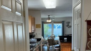 A narrow hallway leading to a kitchen with a dining area, wooden cabinets, and a ceiling fan. - Beachside Vacation Home 117 #B (South Padre Island)