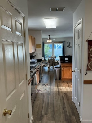 A narrow hallway leading to a kitchen with a dining area, wooden cabinets, and a ceiling fan. - Beachside Vacation Home 117 #B (South Padre Island)
