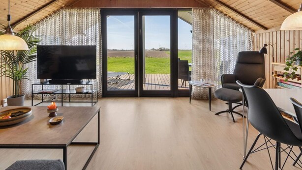 A spacious room with a large TV, a dining table, and a view of the countryside through a sliding door. - 4 Star Holiday Home in Grevinge (Grevinge)