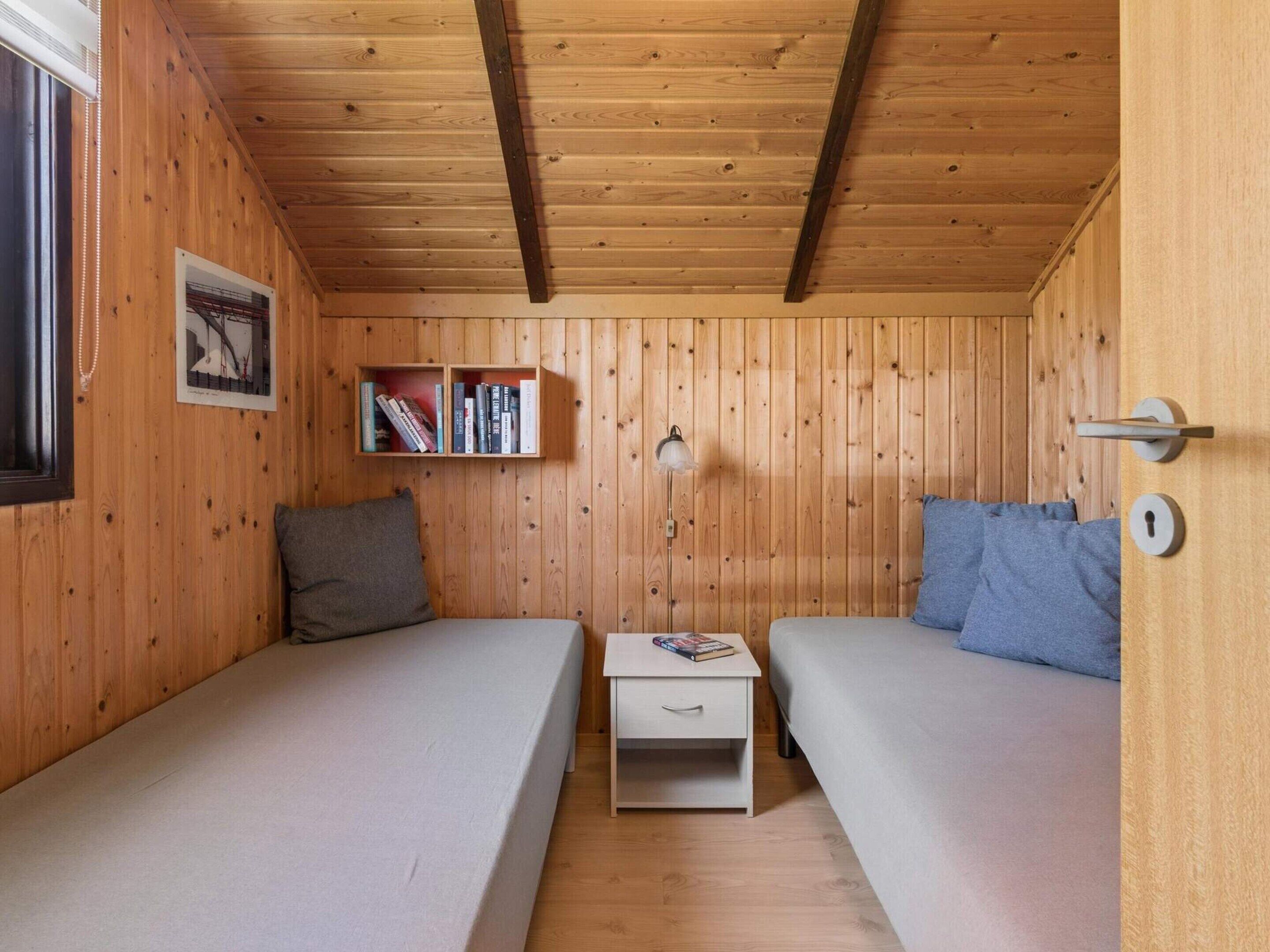 Ein Zimmer mit Holzvertäfelung, zwei Betten, einem Nachttisch, einer Lampe und einer Tür mit Schlüsselloch.