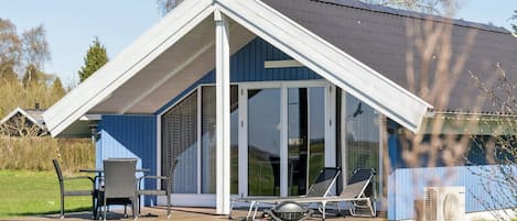 Une maison moderne avec un toit en pente, une terrasse dotée de mobilier d’extérieur et une grande fenêtre.