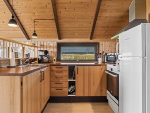 A compact kitchen with wooden cabinetry, a built-in oven, a microwave, and a coffee maker. - 4 Star Holiday Home in Grevinge (Grevinge)