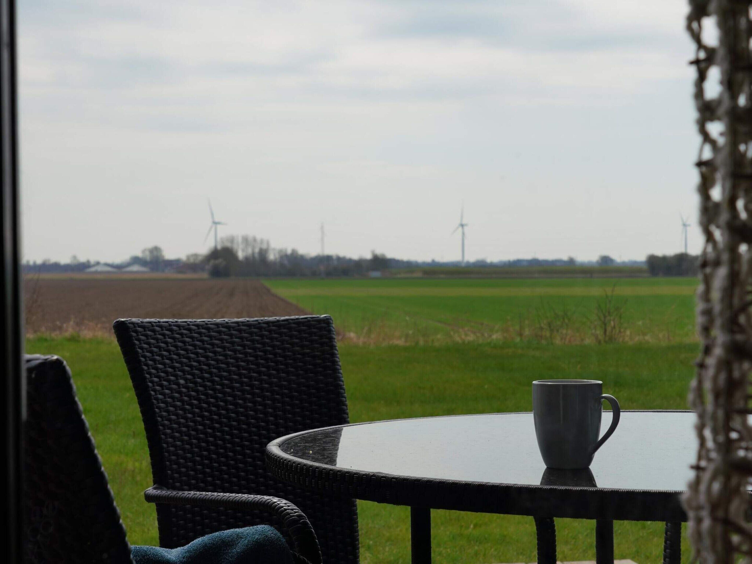 Una silla de mimbre y una mesa con vistas a aerogeneradores y campos.