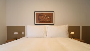 Una cama bien tendida con un edredón escocés, dos lámparas de noche y una obra de arte abstracto enmarcada en la pared.