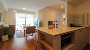 Una cocina moderna con microondas integrado, un comedor con mesa y sillas, y una sala de estar con sofá y planta.