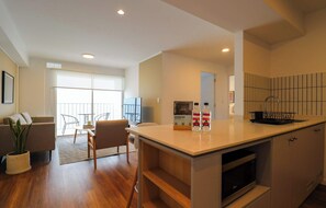 A modern kitchen with a built-in microwave, a dining area with a table and chairs, and a living room with a sofa and a plant. - w* | Upscale 2BR with Balcony in Miraflores (Miraflores)