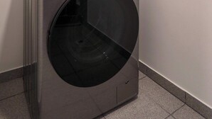 Una lavadora LG ThinQ de carga frontal en un cuarto de lavado con piso de baldosas y pared blanca.