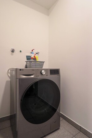 A front-loading LG ThinQ washing machine in a laundry room with a tiled floor and a white wall. - w* | Upscale 2BR with Balcony in Miraflores (Miraflores)