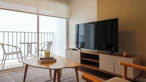 Una sala de estar moderna con un televisor de pantalla plana grande, una mesa de centro de madera, un sofá y un balcón con barandilla.