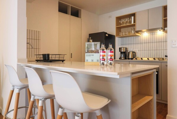 A modern kitchen with a white countertop, bar stools, a coffee machine, and a refrigerator. - w* | Upscale 2BR with Balcony in Miraflores (Miraflores)