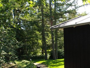 Eine Holzhütte mit geneigtem Dach, umgeben von dichtem Grünwerk und Bäumen.