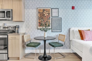 Une cuisine moderne équipée d’appareils électroménagers en acier inoxydable, un coin repas avec une table ronde et deux chaises, et un canapé blanc agrémenté de coussins à motifs.