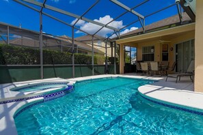 Une piscine au design incurvé, un patio couvert avec des chaises, et une vue sur les maisons voisines.