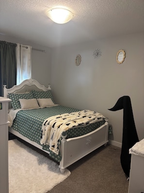 Ein Schlafzimmer mit einem Bett, einem weißen Schminktisch, einem schwarzen Kleiderbügel und zwei Wandspiegeln.