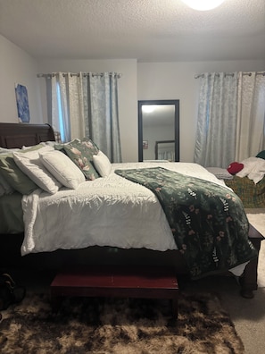 Ein Schlafzimmer mit Bett, einer Bank, einem Spiegel und Vorhängen.