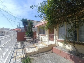Ein Wohngebäude mit geschlossenem Eingangsbereich, einer kleinen Veranda und einer gefliesten Terrasse.